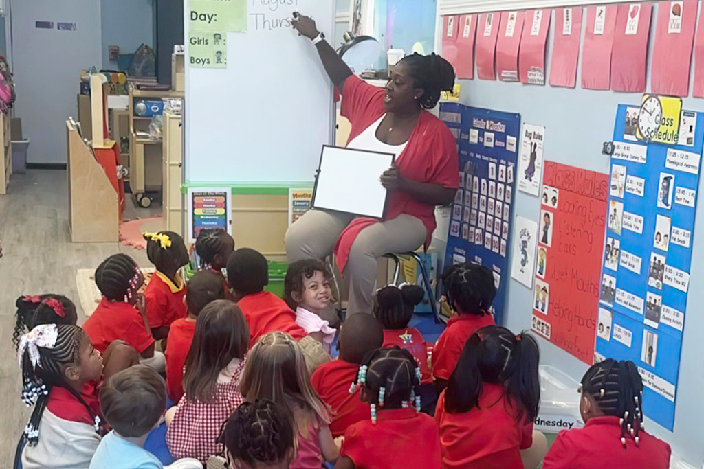 A teacher leads a lesson as young students attentively listen, creating a lively and engaging classroom atmosphere.