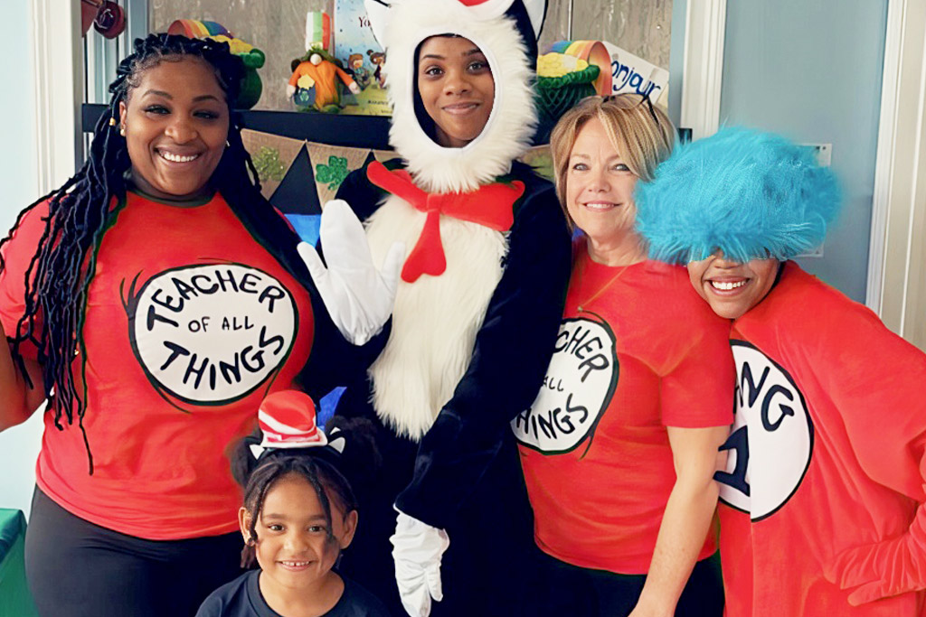 A group of teachers and a child dress up in fun costumes, celebrating creativity and joy in a vibrant classroom setting.