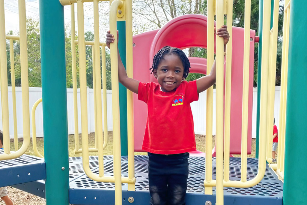 A smiling child in a red shirt plays on a colorful playground, showcasing joy and active outdoor fun.