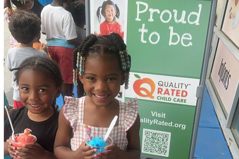 Two girls smile brightly holding cups of colorful ice cream, showcasing their joyful moment