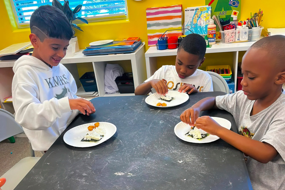 Three children are engaged in a creative activity, carefully assembling ingredients on plates.