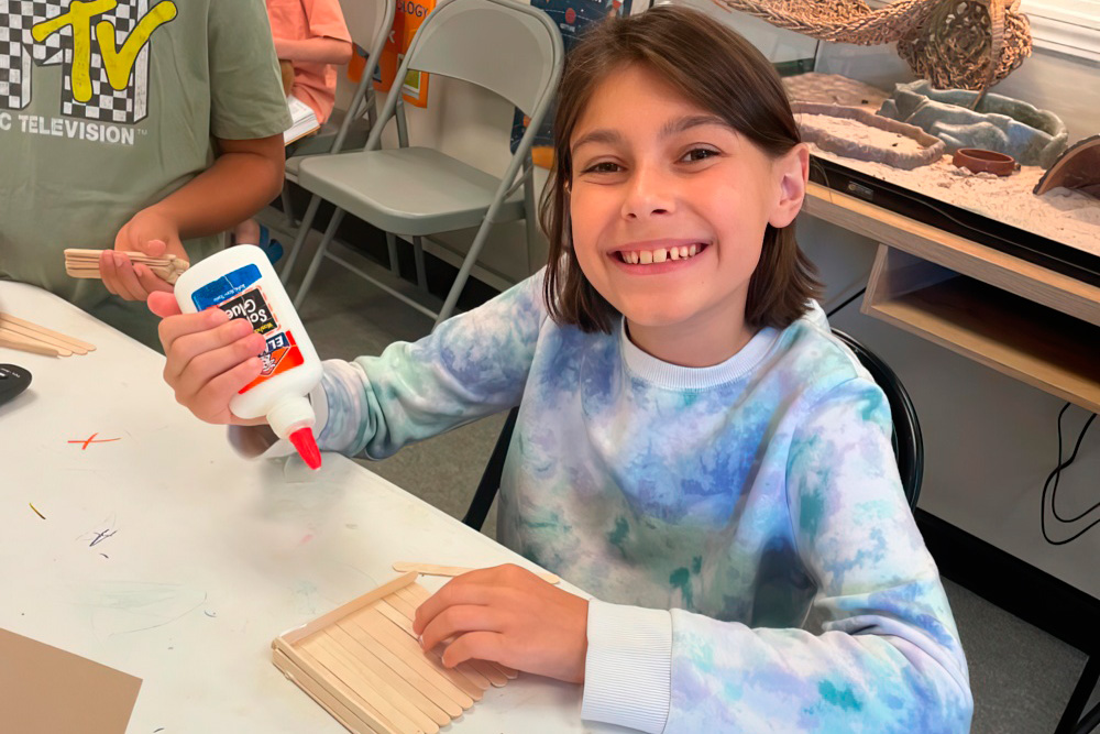 A smiling girl engages in a craft activity, holding glue and showcasing her creativity.