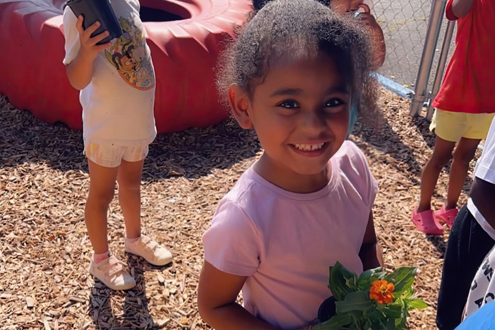 A smiling girl holds a bouquet of flowers in a sunny playground, creating a joyful scene.