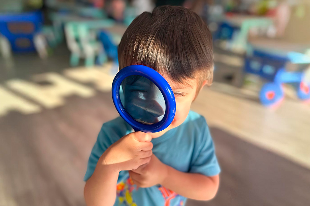 A child holds a magnifying glass, playfully examining the world around them with curiosity and wonder