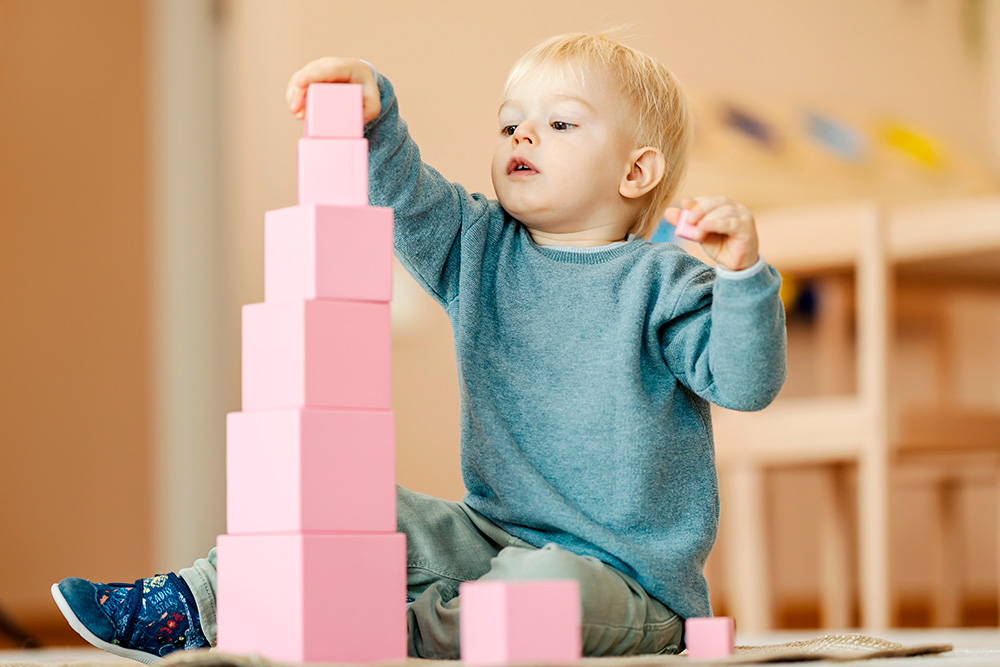 A young child is focused on stacking pink blocks, showcasing concentration and creativity in a playful environment.