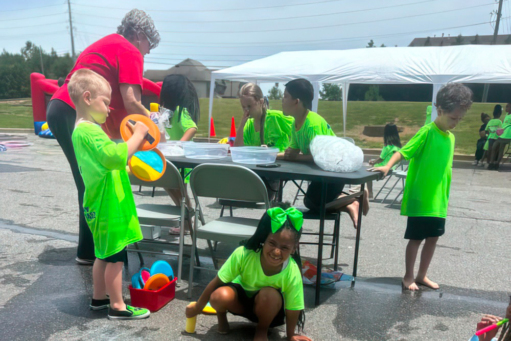 Children in bright green shirts play and engage in water activities at a fun outdoor with a teacher