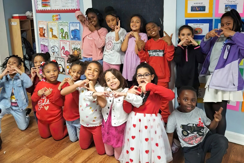 A cheerful group of children poses together, making heart shapes with their hands, surrounded by a warm atmosphere.