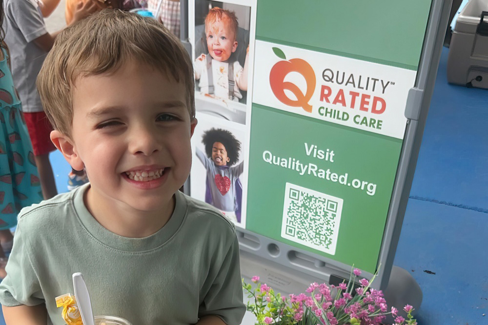 A young boy holding a cup of ice cream standing in front of a quality-rated child care, radiating happiness and excitement.